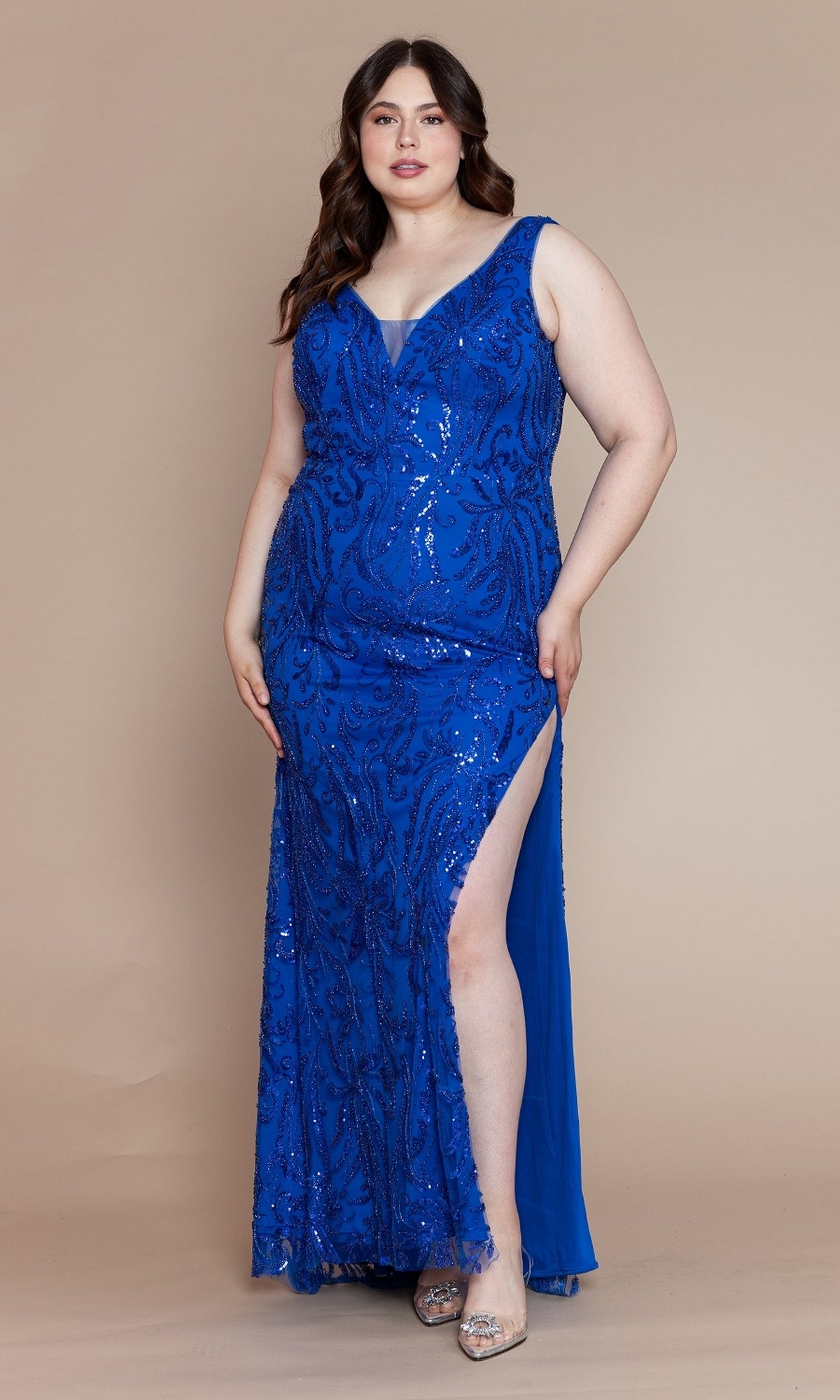 A woman stands against a plain beige background wearing the Glitter-Print Long Plus-Size Prom Dress W1140, featuring royal blue color, sleeveless design, sequins, and a thigh-high slit.